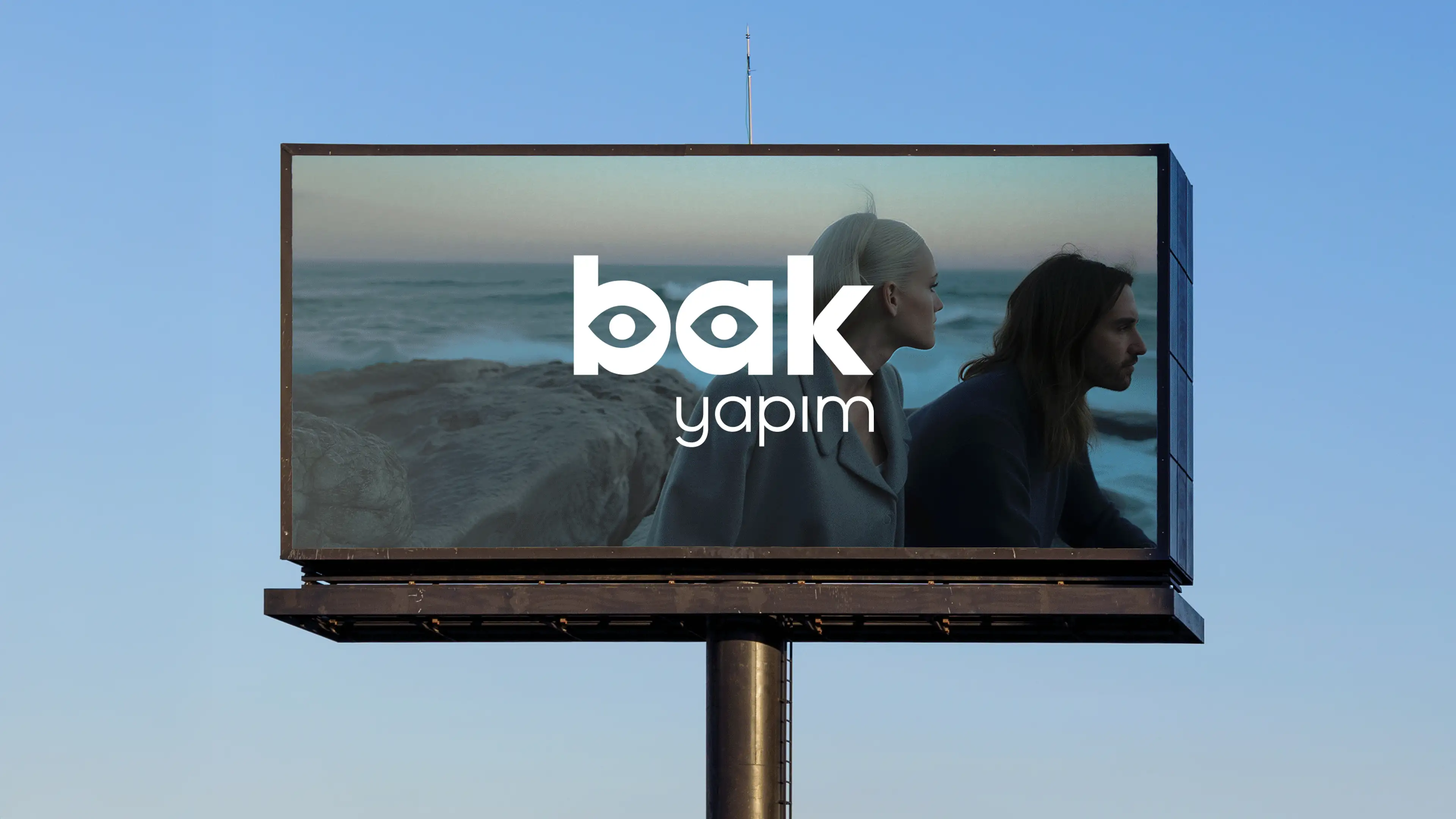 Large outdoor billboard displaying the Bak Yapım logo overlaid on a cinematic brand image against a clear blue sky.