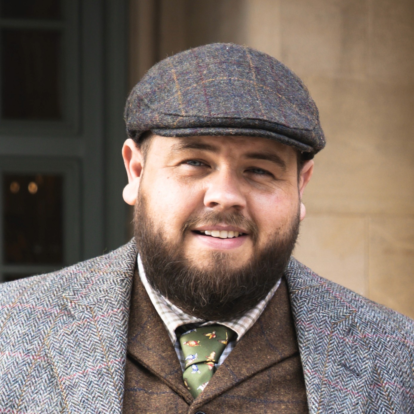 man wears smart tweed clothing with blue jacket, dickie-bow flat cap and glasses in the derbyshire countryside