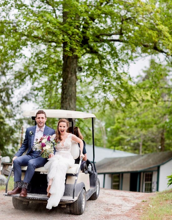 Newlyweds smiling on a golf cart under the trees at Camp Lenox
