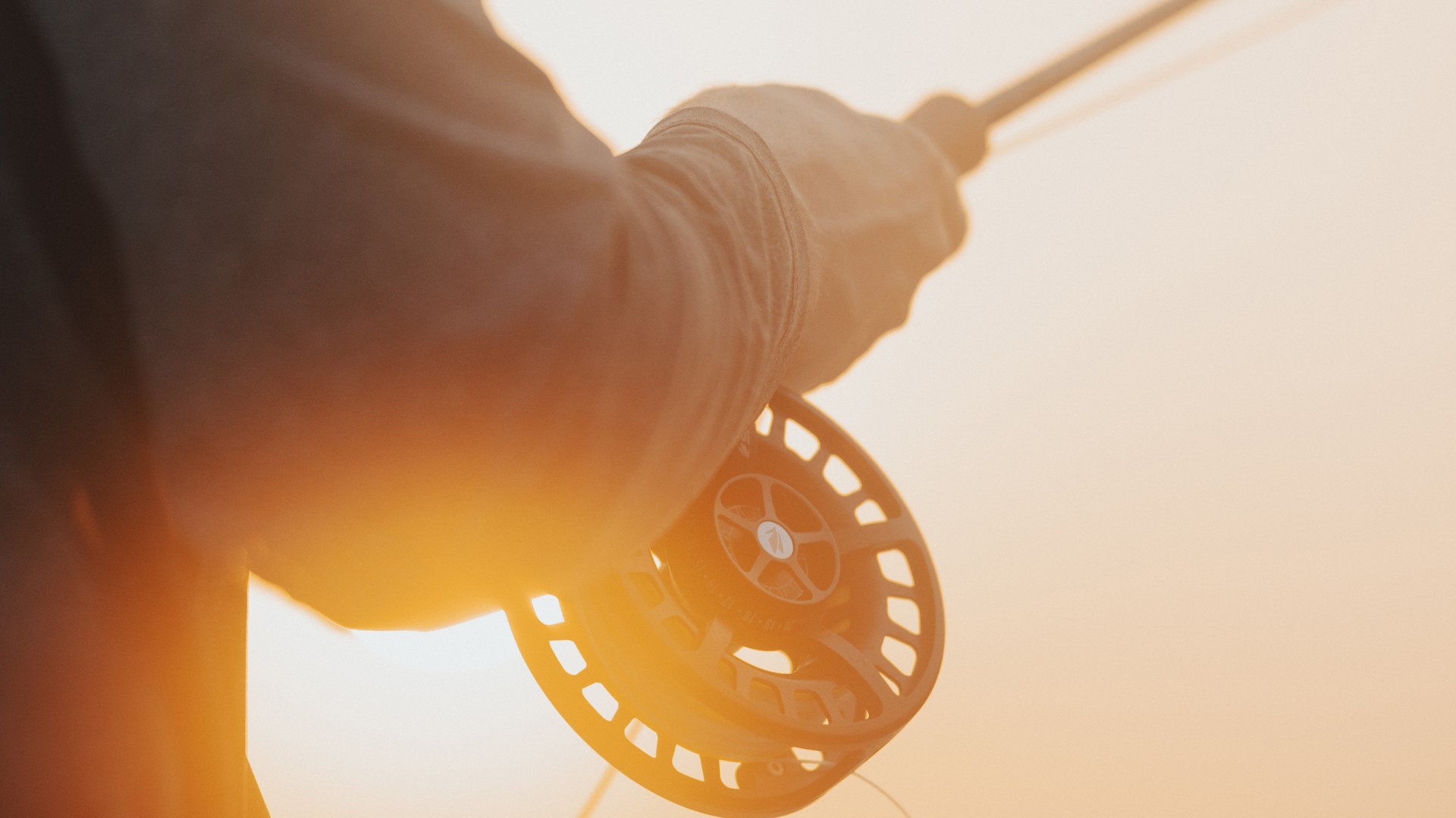 Closeup of a fly reel and an angler holding it during sunset