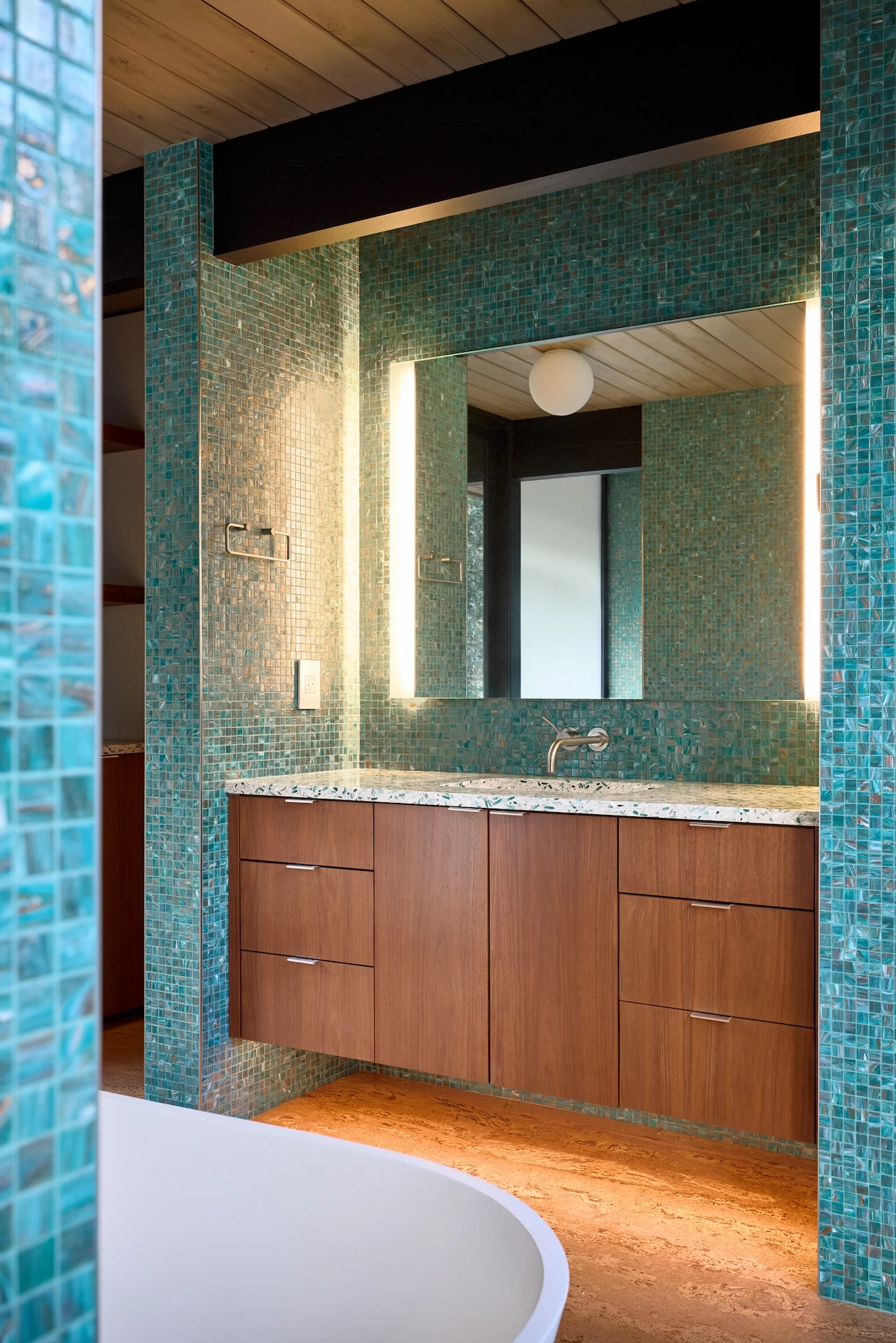 Portrait of the master bathroom's floating vanity, illuminated by LED floor lighting, highlighting the modern amenities in this historical Eichler home. Photo by Todd Huge.