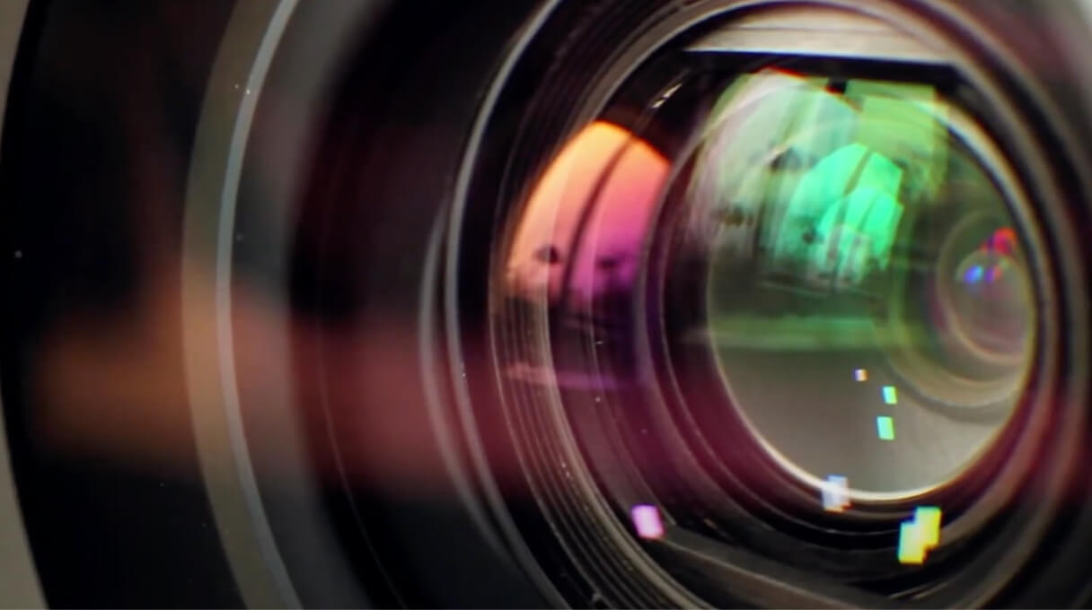 Close-up of a camera lens with reflections and colorful highlights, emphasizing its intricate glass elements.