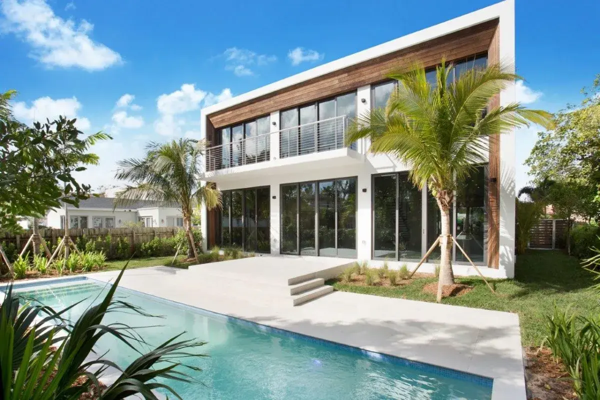 Poolside view of modern two-story residence with wood cladding and open terrace in Miami Beach by Atelier International LLC