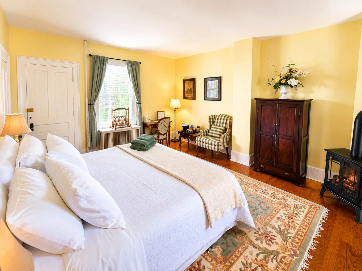 Cozy bedroom with white bed, two red chairs, fireplace, door open to garden.