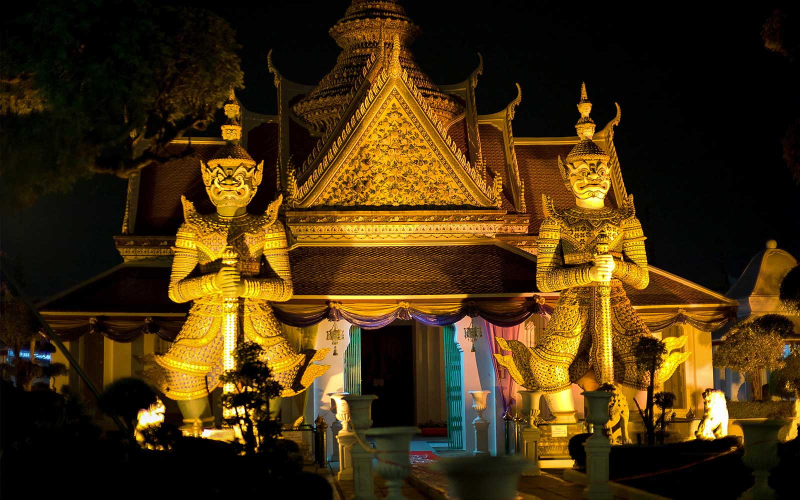 Statuy gigantycznych strażników w świątyni Wat Arun, oświetlone nocą, Bangkok Night Bike Tour.
