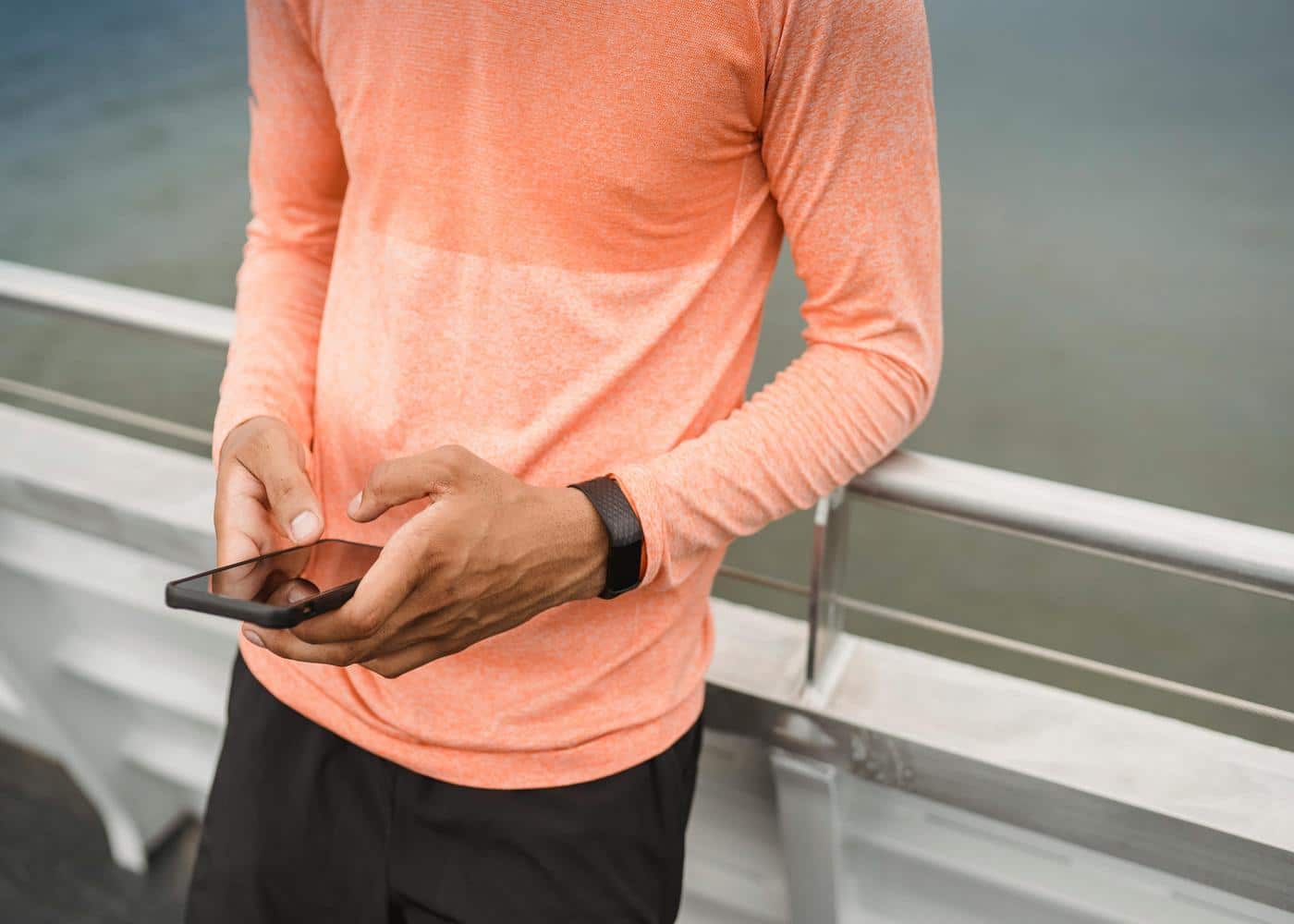 Man in activewear wearing smartwatch and looking at smartphone