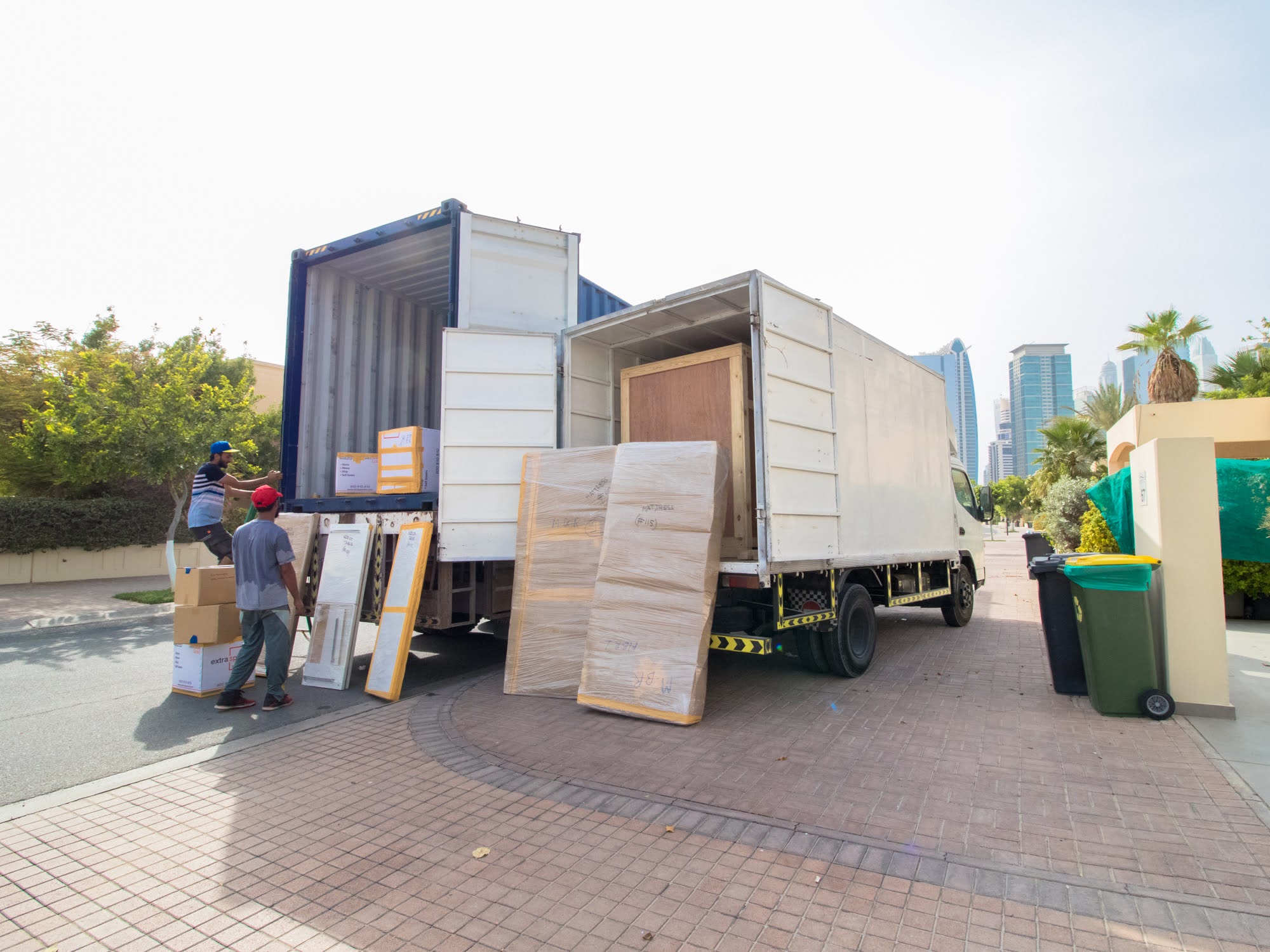 Trucks unloading furniture and boxes near high-rises for storage facility Dubai service.