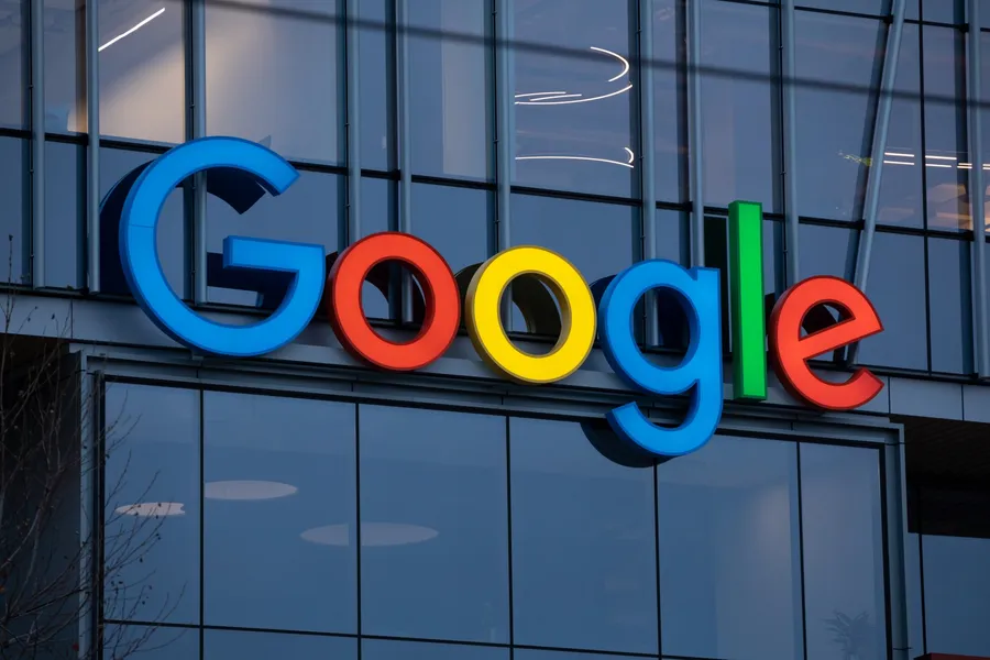 Google logo in colorful letters mounted on the exterior of a modern office building with glass windows.