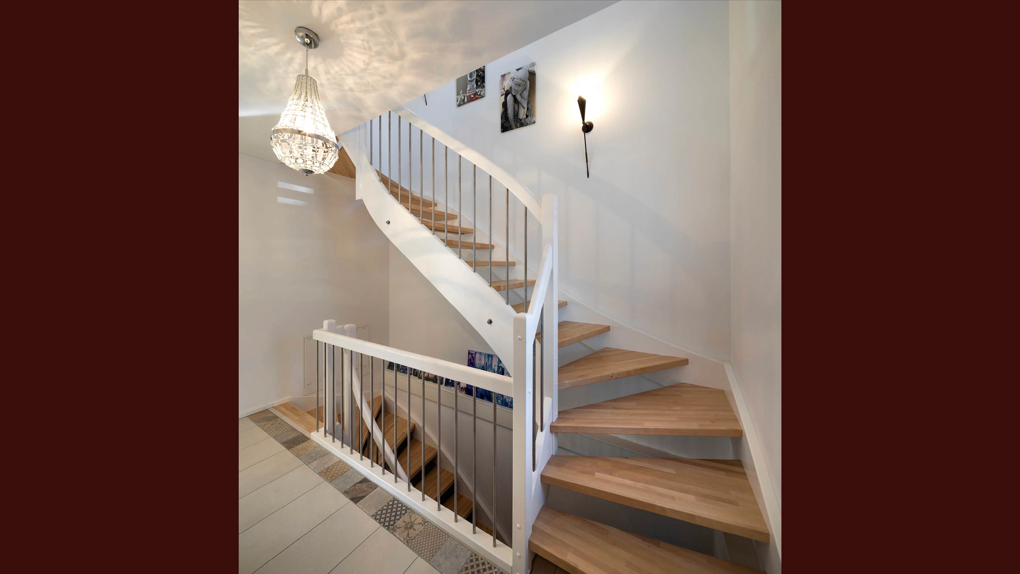 Windeltreppe mit Holzstufen und weißem Geländer. Ein Kronleuchter hängt von der Decke, daneben eine Wandleuchte.