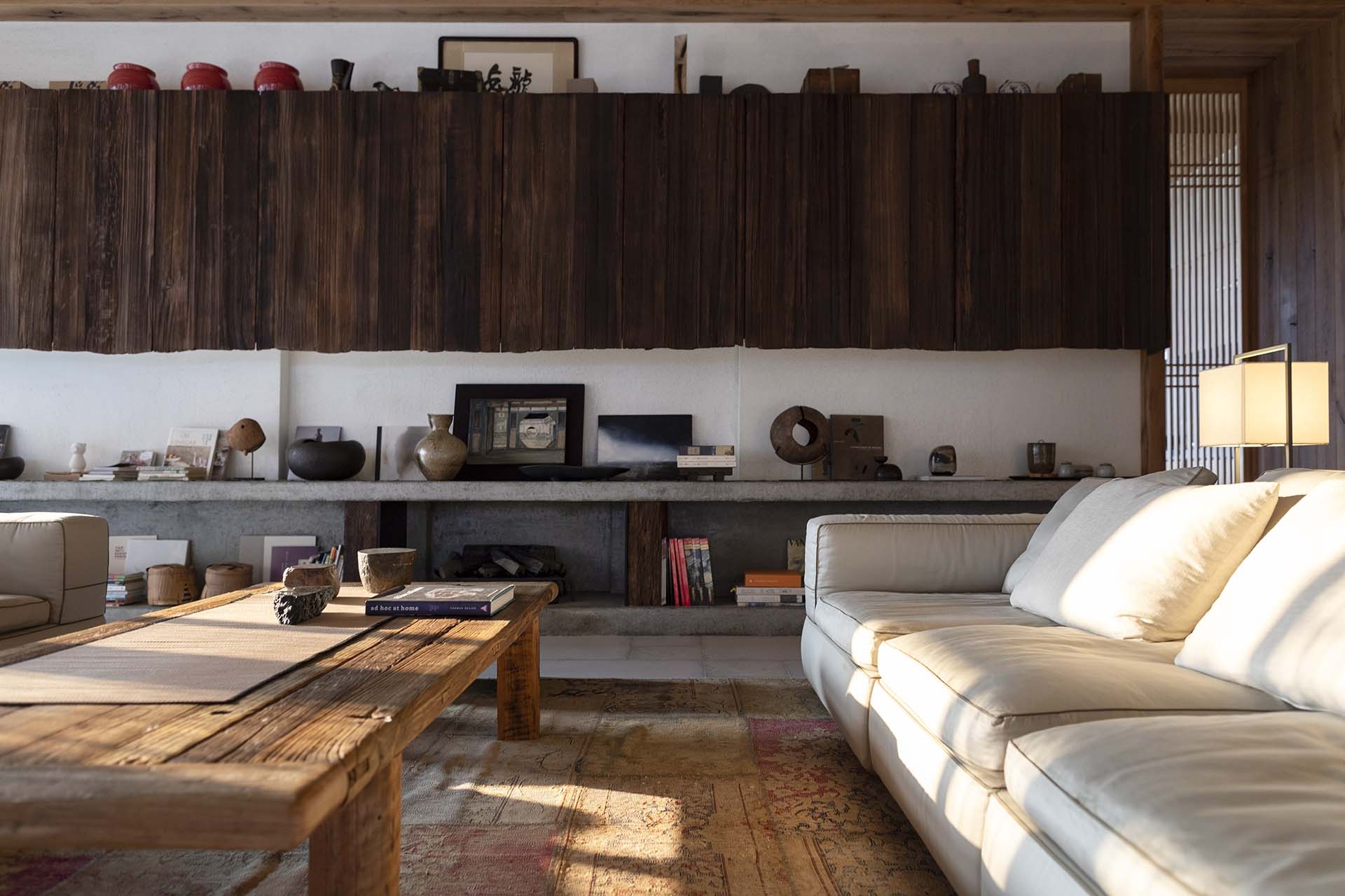 侘寂風格客廳搭配米白沙發與木質茶几，書籍與陶器陳列於展示平台上，自然光灑落空間