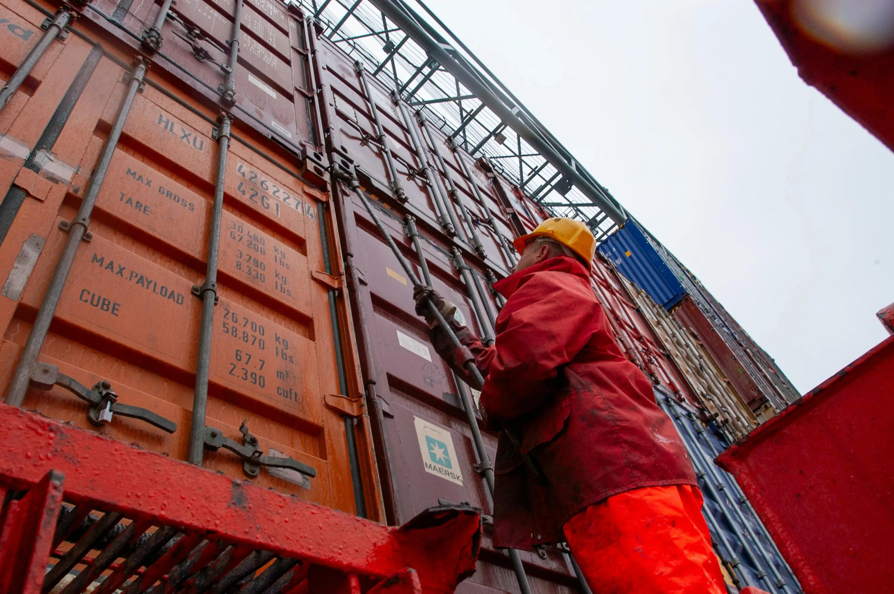 Dockworker in safety gear climbing stacked shipping containers