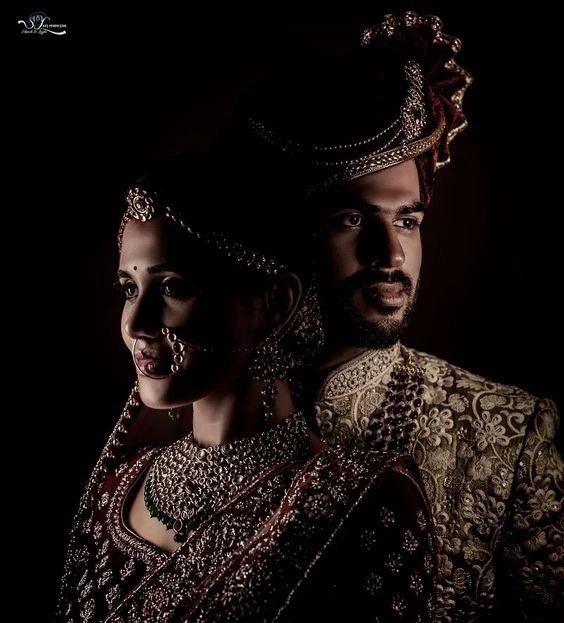 Dramatic, low-light portrait of bride and groom in traditional attire, with intricate jewelry and textures highlighted, evoking a sense of timeless elegance, captured by Out of The Blues Fine Art Wedding Photography in Hyderabad.