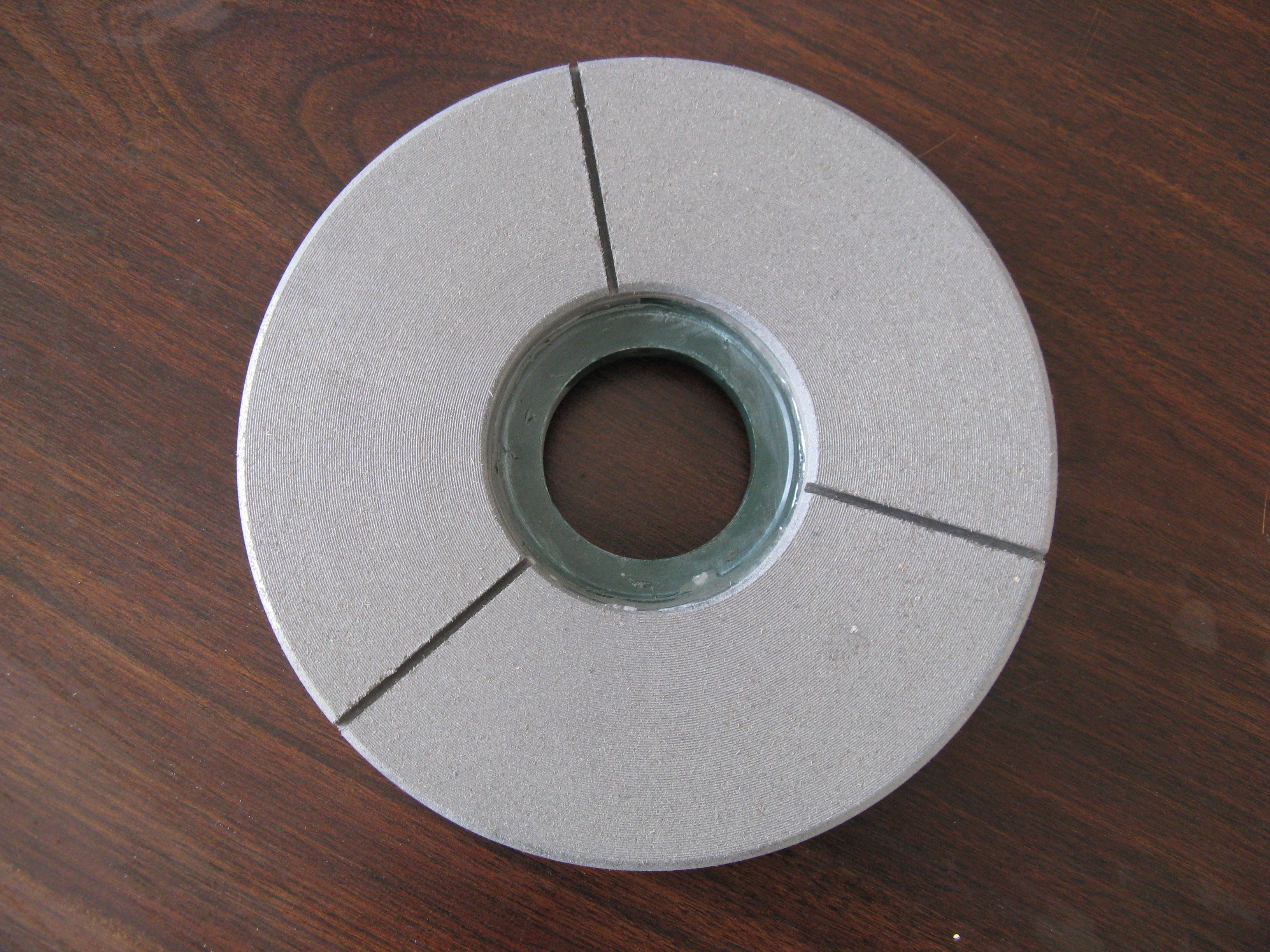 A gray polishing disc with a green center, displayed flat on a wooden surface.