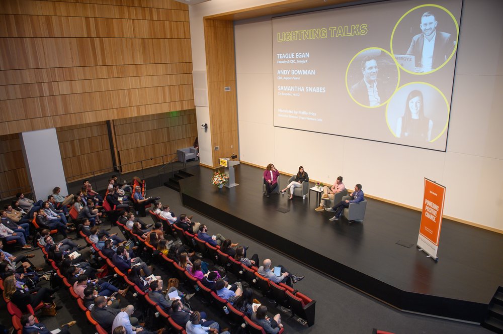 A conference hall with a speaker at the front and an audience seated, engaged in a presentation.
