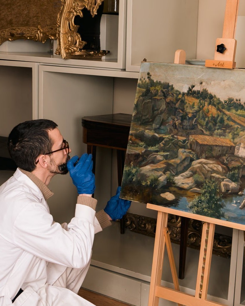 Conservador-restaurador a analisar pintura de paisagem no atelier Patrimonium, Porto