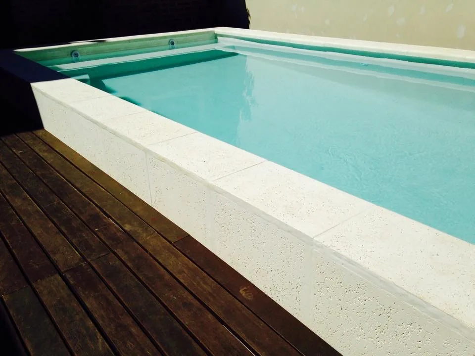Diseño de piscina elevada con borde atérmico blanco puro, revestida interiormente en Aquavations, acompañada de un elegante deck de madera natural.