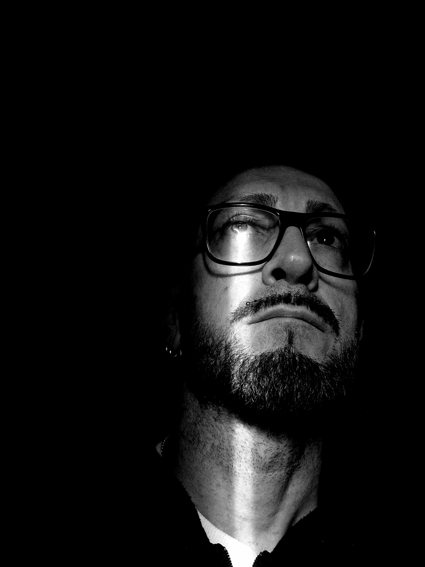 Artistic portrait of contemporary artist Mavro, captured from a low angle looking upwards in high-contrast chiaroscuro. This image represents the artist's creative journey and ongoing research, accompanying the Bio and CV section of Mavro Studio.