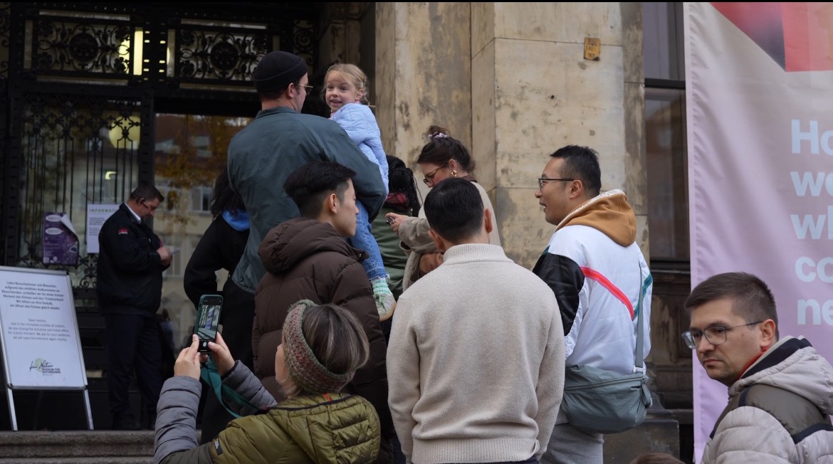A large group photo of diverse team members gathered in an industrial-style space with arched ceiling.