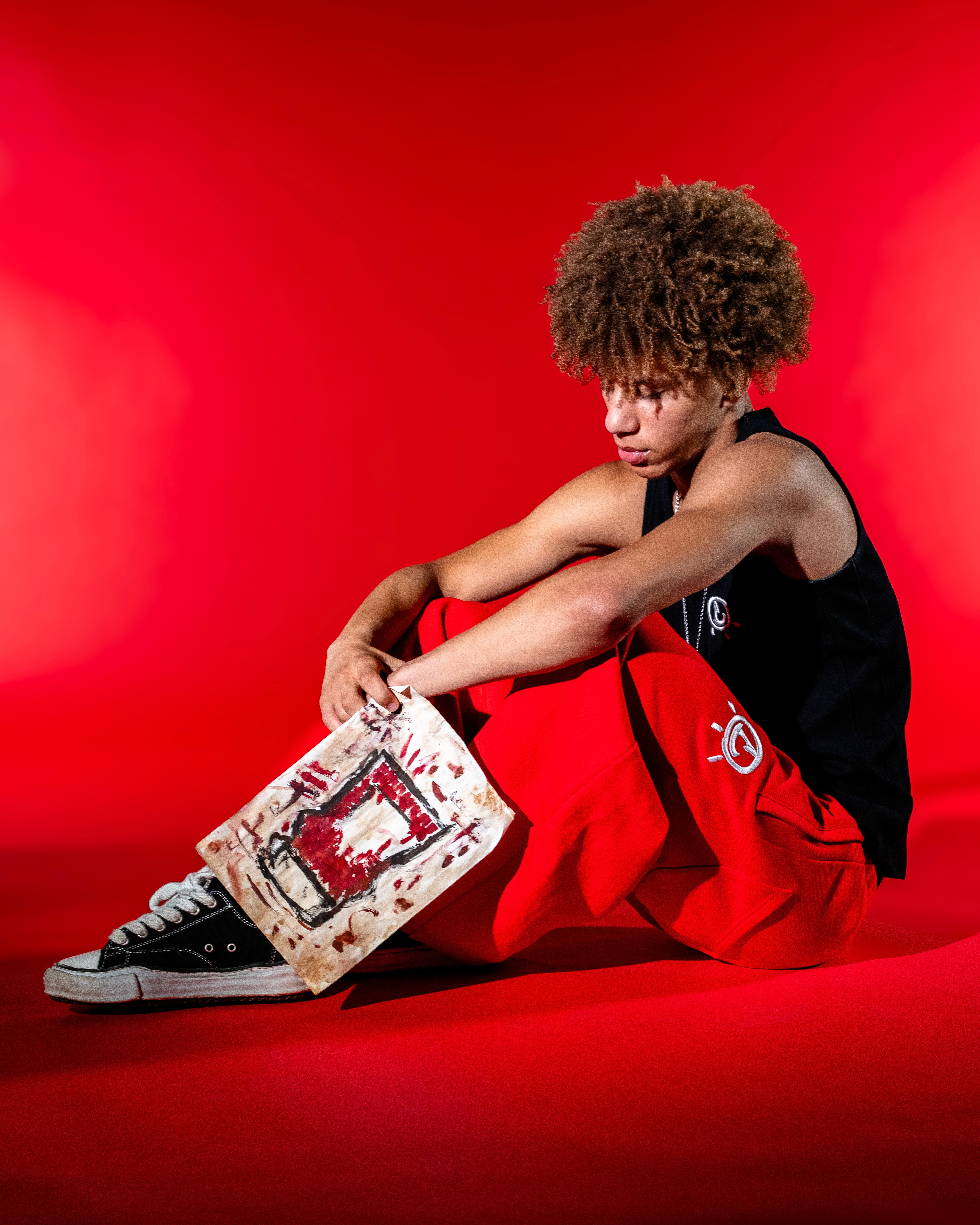 Smiling man in a white hoodie and black pants standing confidently on a bright green football field with empty stadium seats behind.