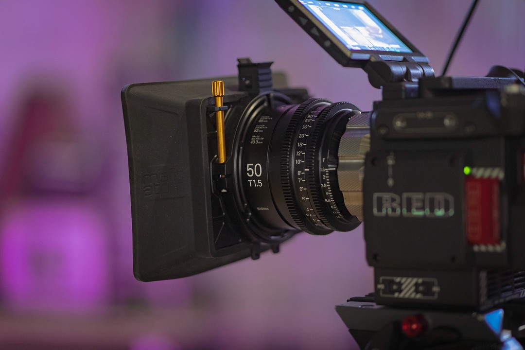 RED branded cinema camera with attached lens on a pink background
