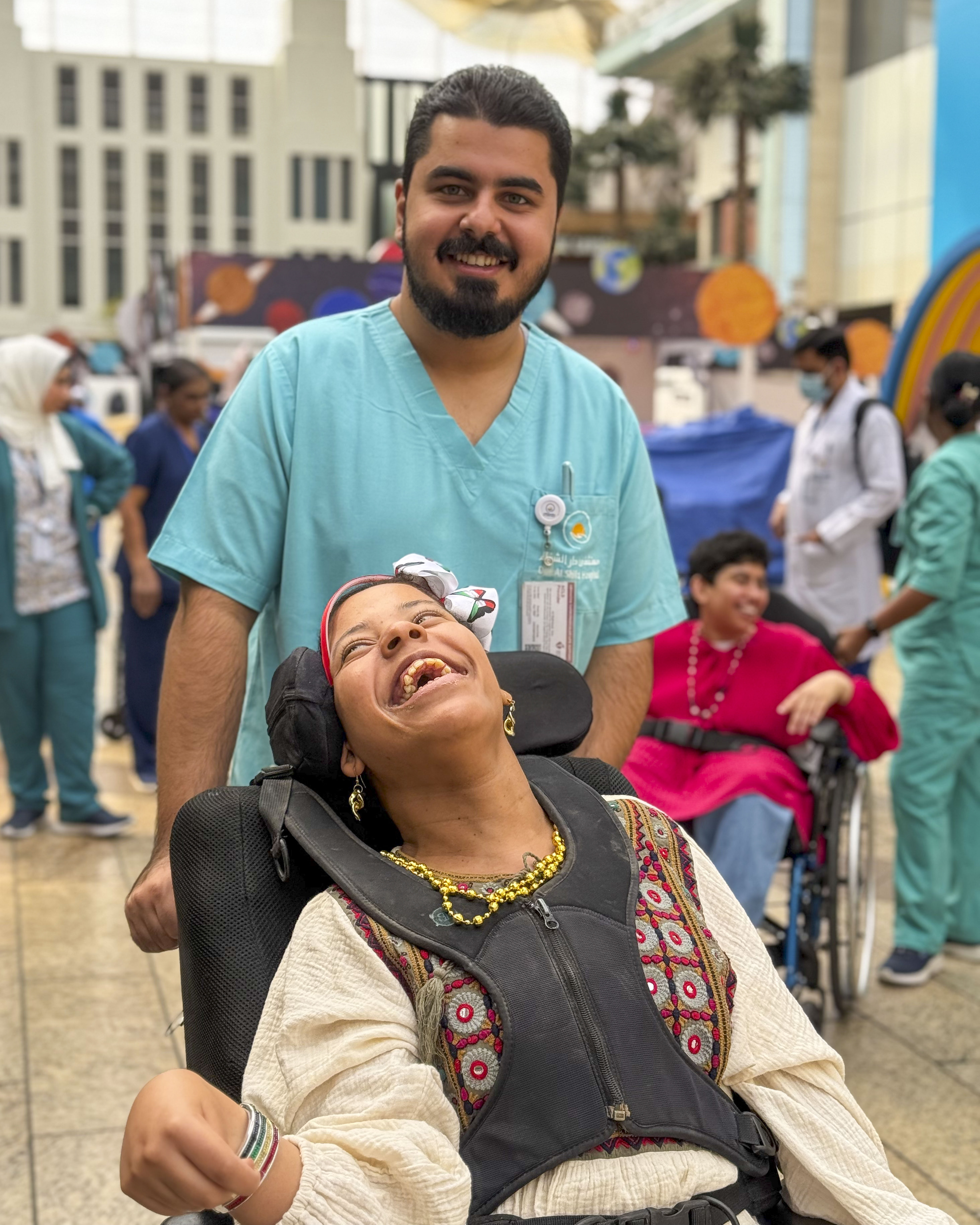 Una persona con una camiseta negra y pantalones de color claro está de pie en la cima rocosa de una montaña al atardecer, sosteniendo una cámara frente a su cara para tomar una foto. Un mar de nubes se extiende detrás de ellos, iluminado por la luz dorada del sol poniente.
