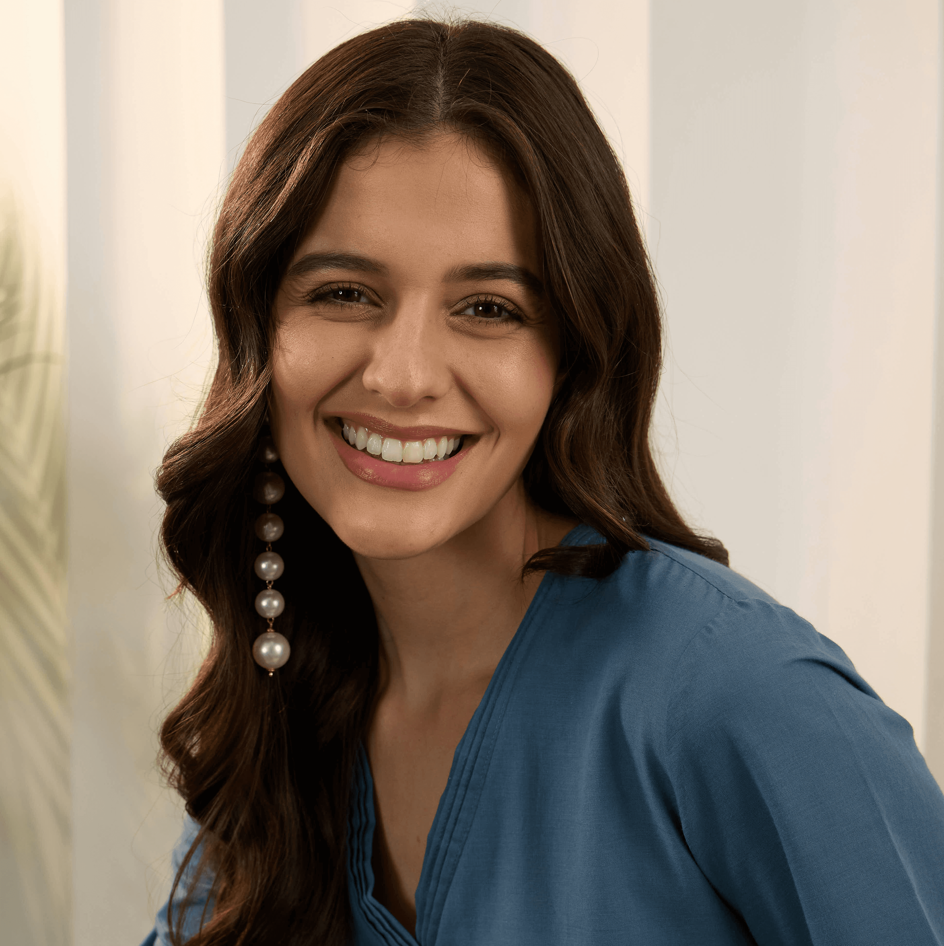 A young woman with dark wavy hair smiles brightly smiling