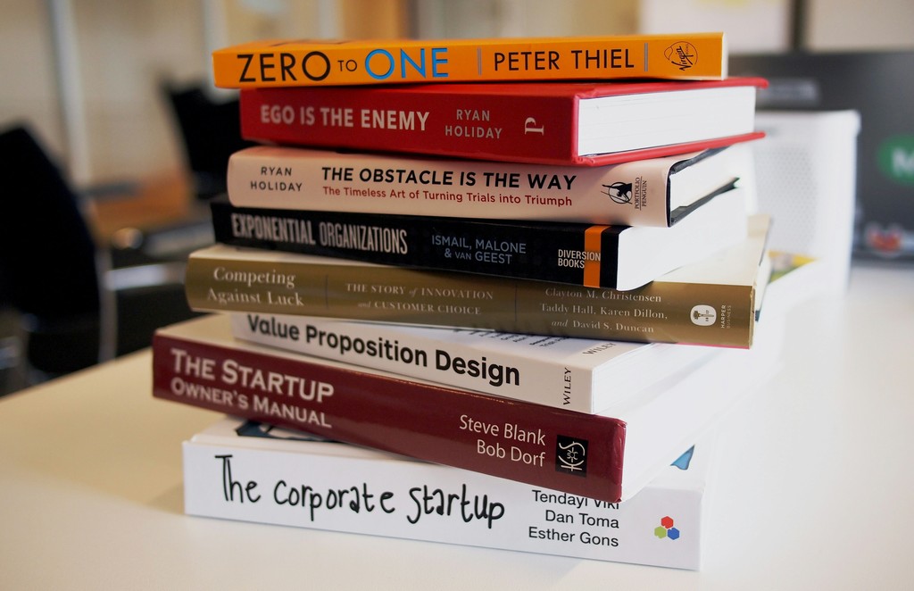 A stack of business and self-improvement books, including titles like "Zero to One," "Ego is the Enemy," and "The Startup Owner's Manual," emphasizes themes of entrepreneurship, innovation, and personal growth, making it a valuable resource for aspiring entrepreneurs and business professionals.   2/2