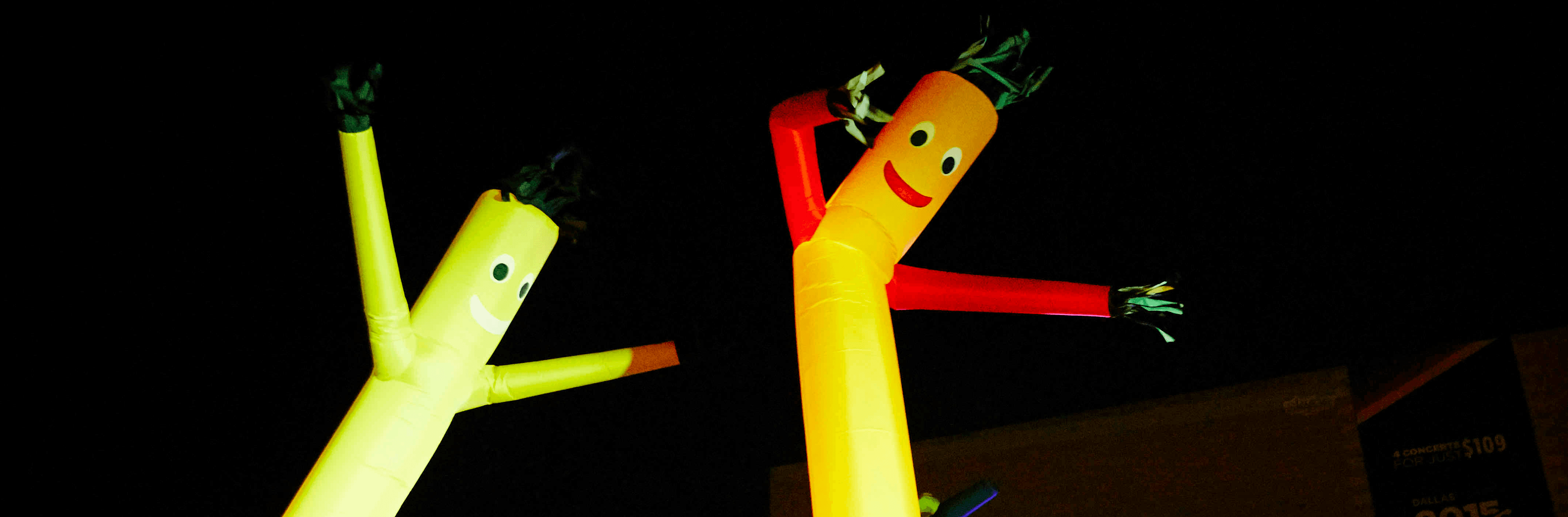 Brightly colored inflatable tube men dancing in a nighttime setting with colorful lights in the background.