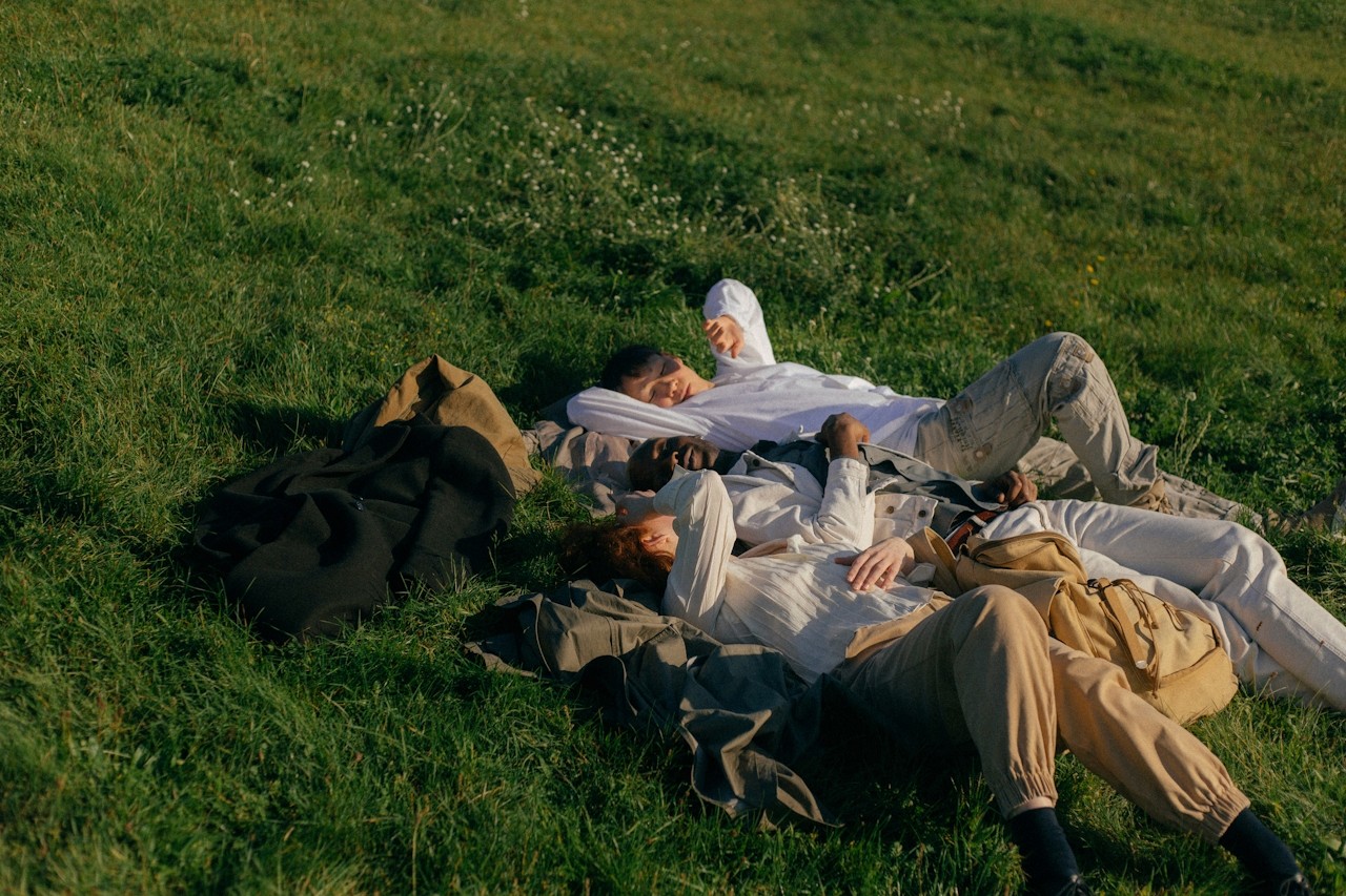 Three people lying down on the green grass, relaxing outdoors.