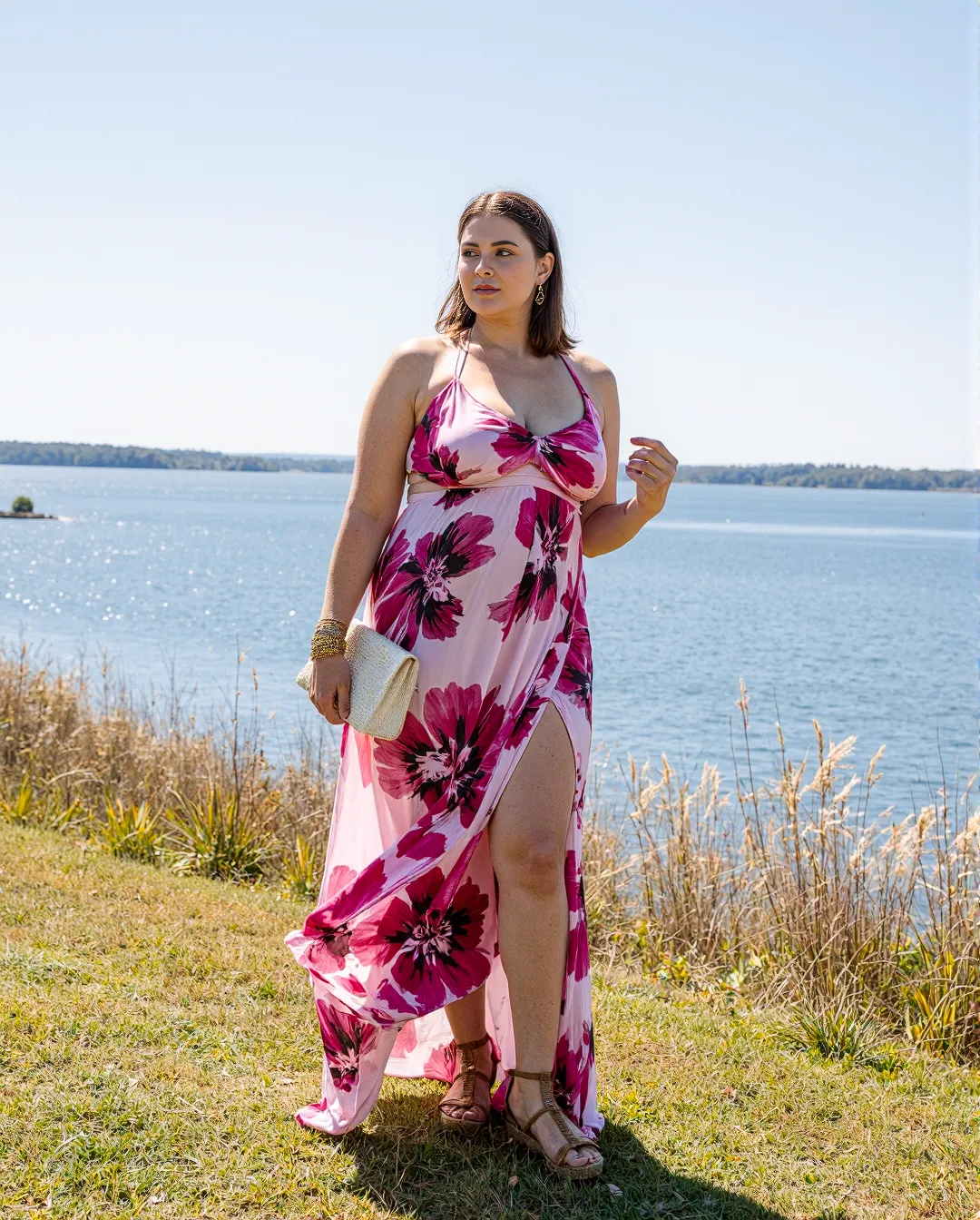 Floral pink maxi dress with side slit captured in bright sunlight by a serene lake, showcasing summer fashion against nature