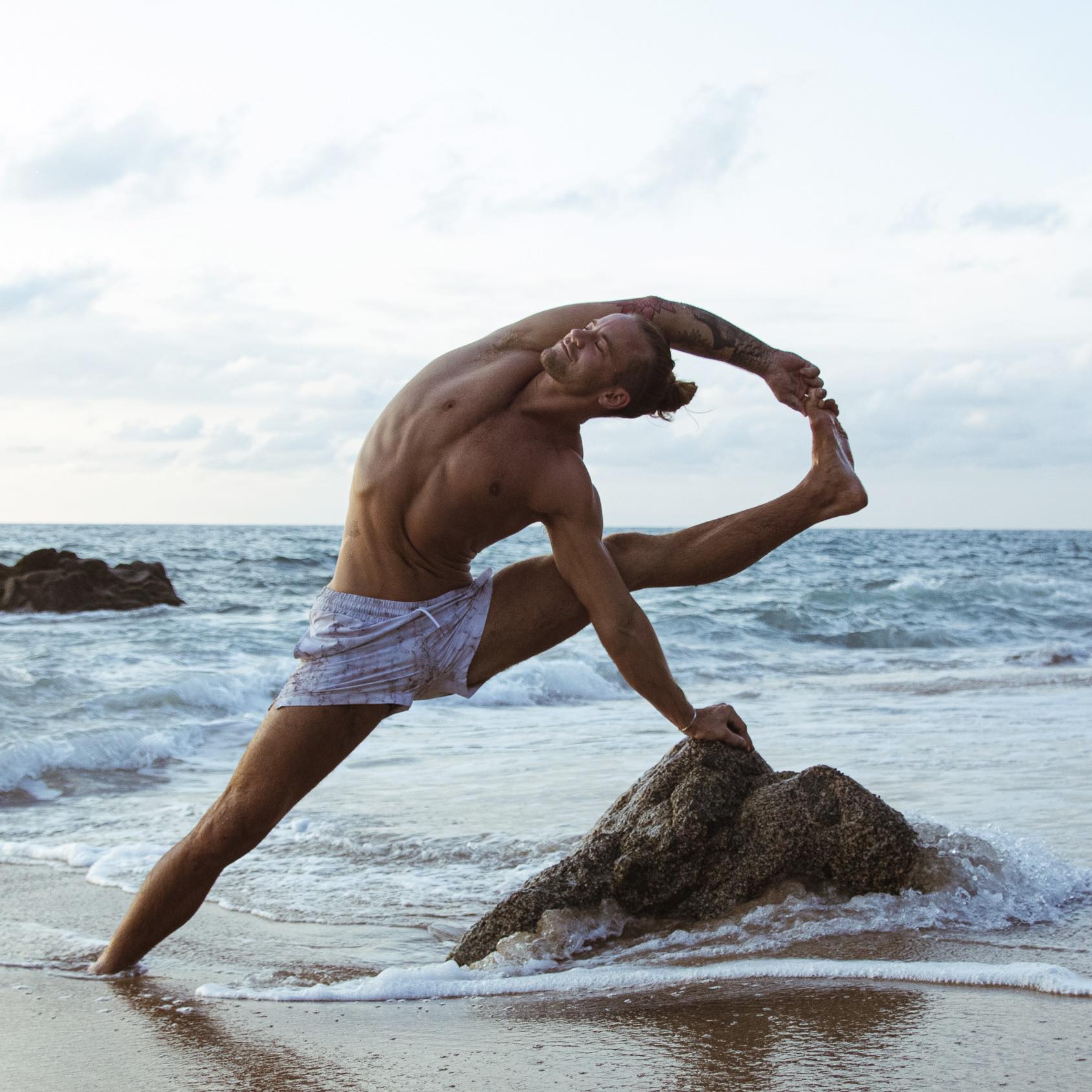 Smiling woman in beige yoga outfit sitting in natural light with green plants in the background.