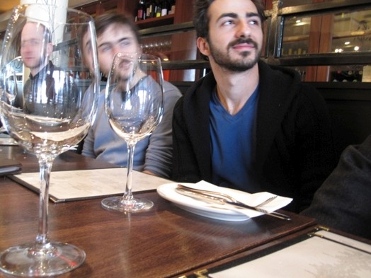 A photo of a group of people sitting next to each other at a restaurant table and watching something.