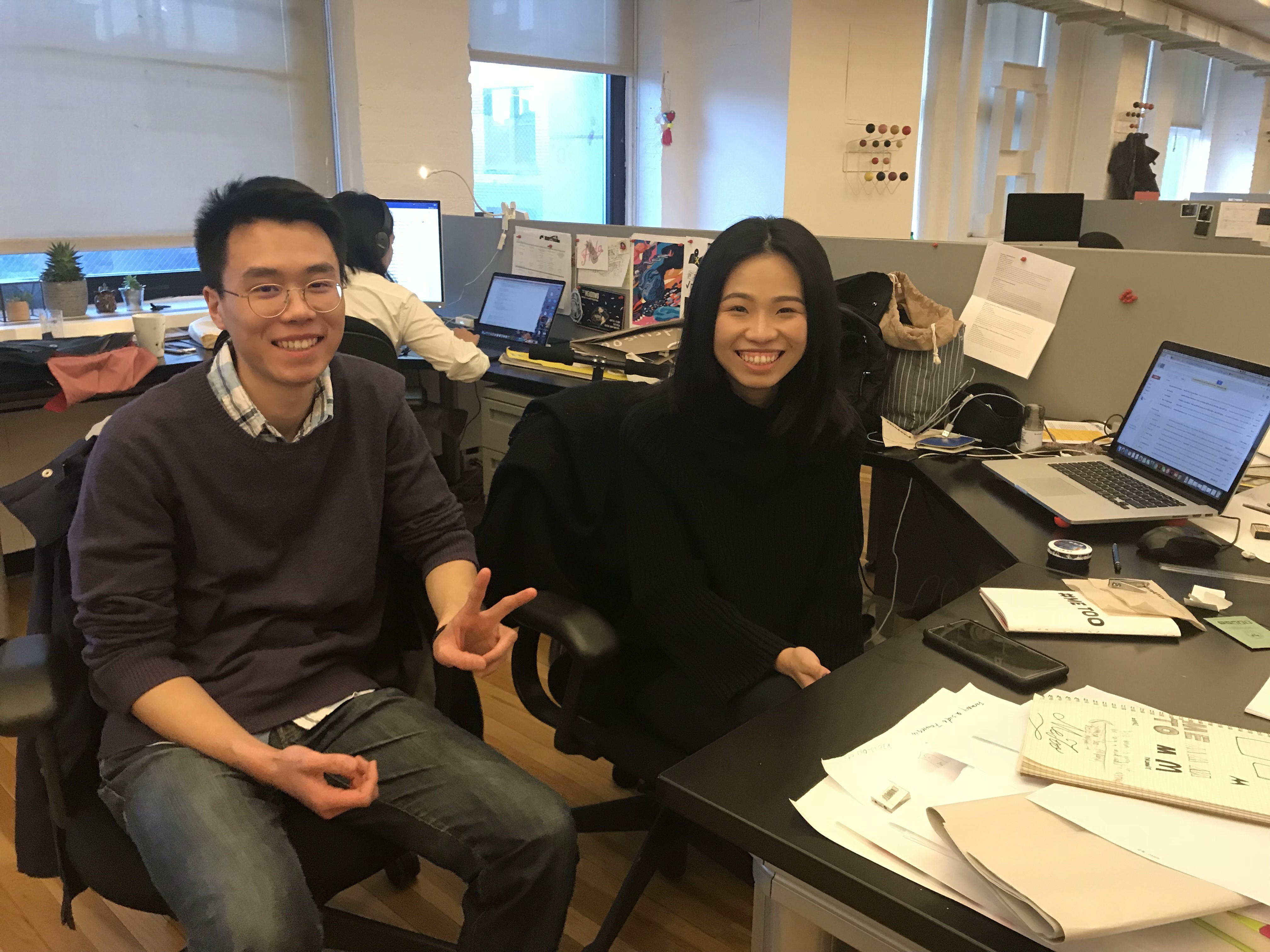 A photo of two people sitting in an office near a desk filled with papers and laptops.