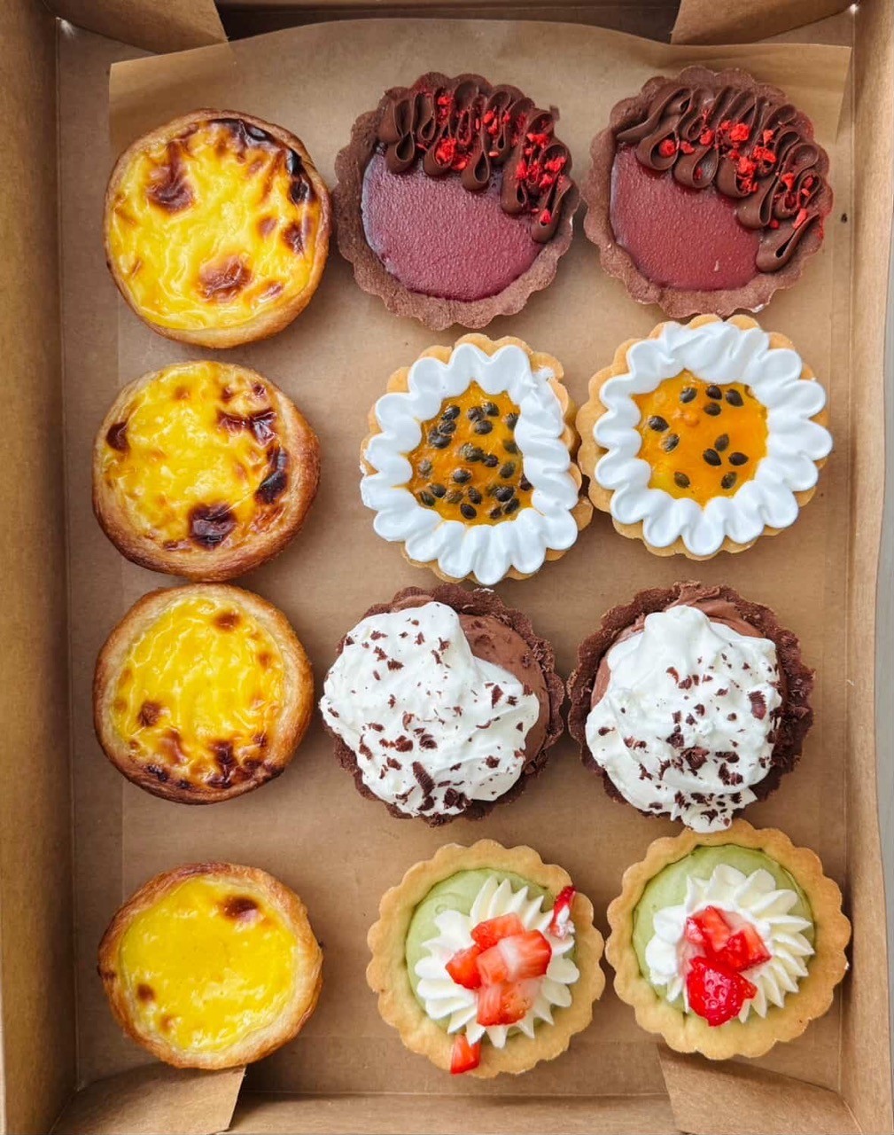A variety of Cadinho bakery tarts in a brown box