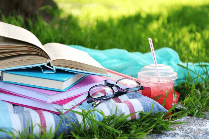 High school student working on a research paper at a desk during summer, surrounded by books and a laptop