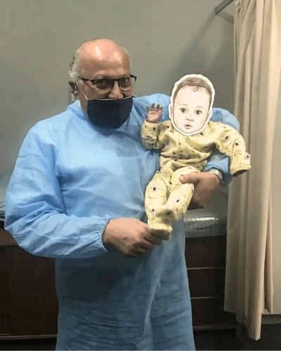 Dr. Ashraf Saddik in surgical scrubs holding a baby at his Melbourne circumcision clinic.