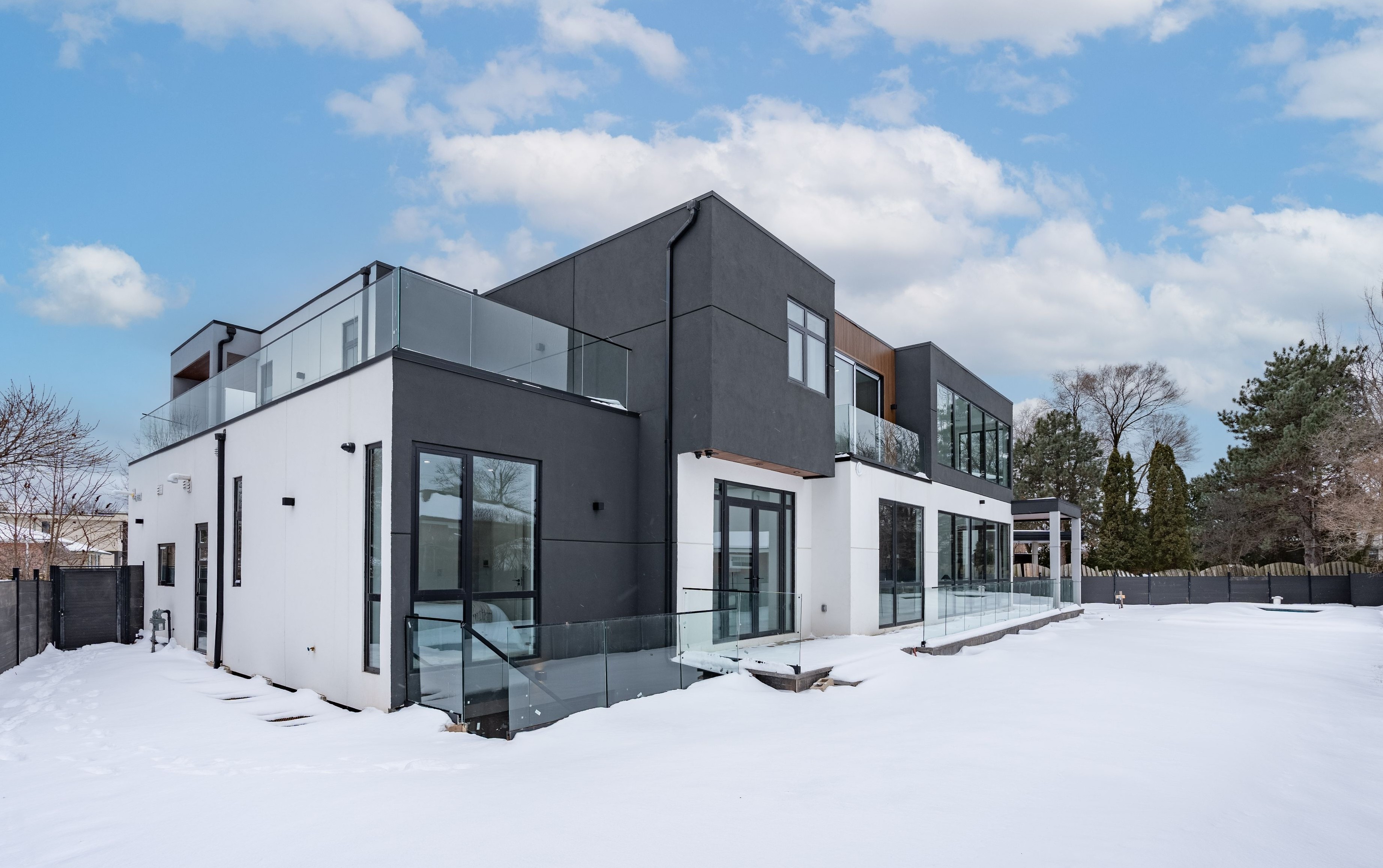 A modern, minimalist cliffside house with large glass windows offers stunning ocean views, surrounded by lush greenery and bathed in warm sunlight.