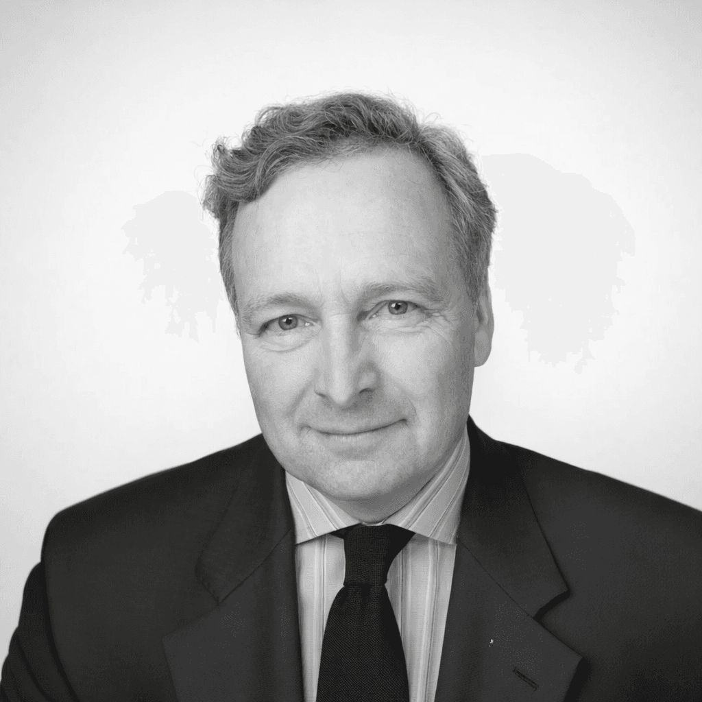 A person with medium-length brown hair wearing a dark, textured coat and a burgundy turtleneck. They have a calm, neutral expression.