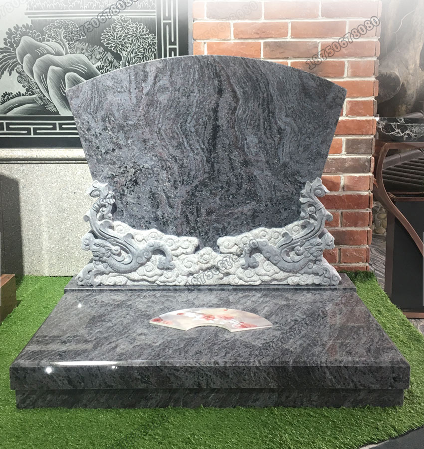 A black granite tombstone with intricate dragon carvings on the lower portion. The tombstone is set on a green artificial grass base, enhancing the contrast between the stone and its surroundings.