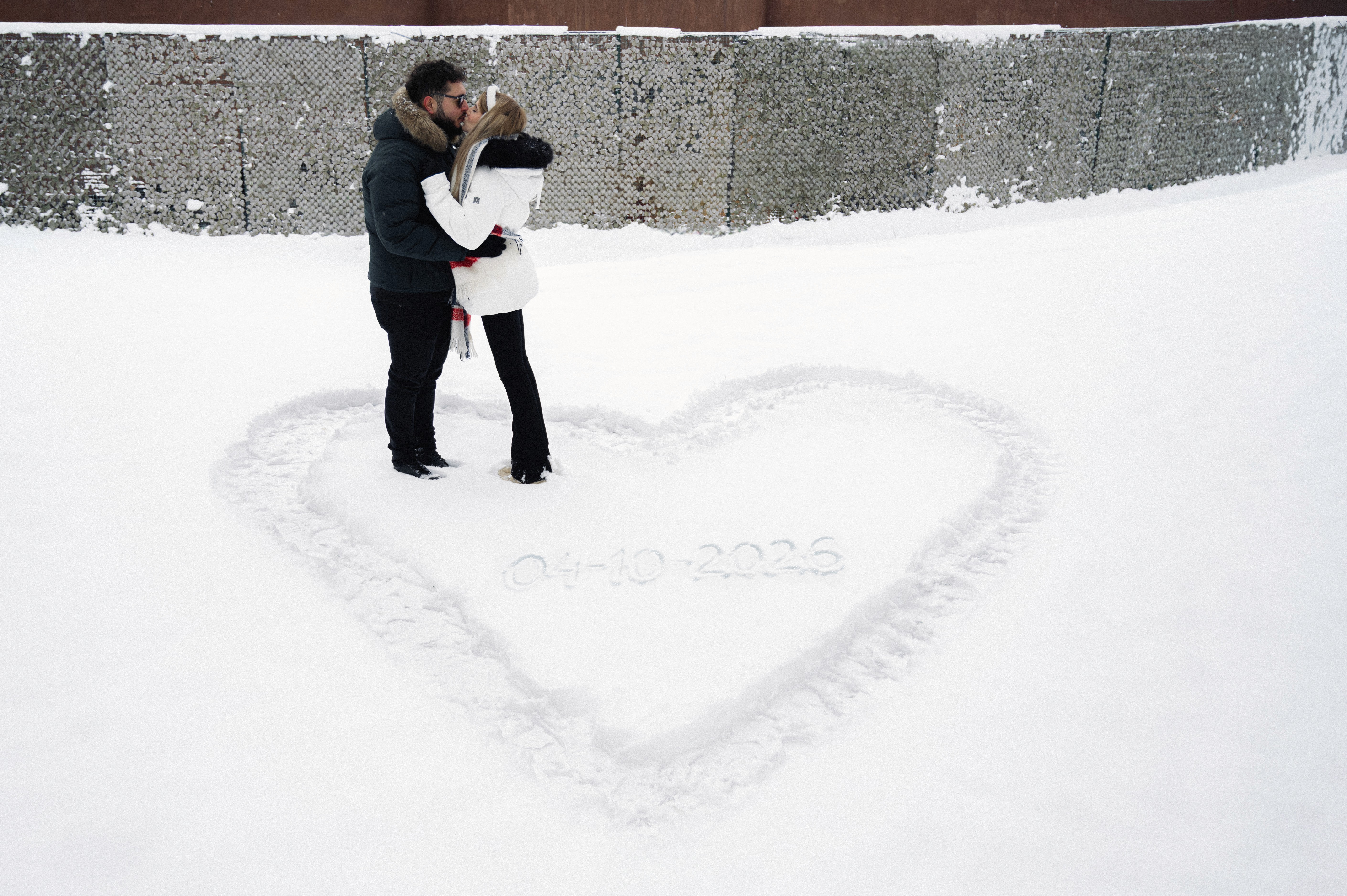Cuplu într-o ședință foto Save the Date de iarnă, fotografiat de sus, cu inimă desenată în zăpadă