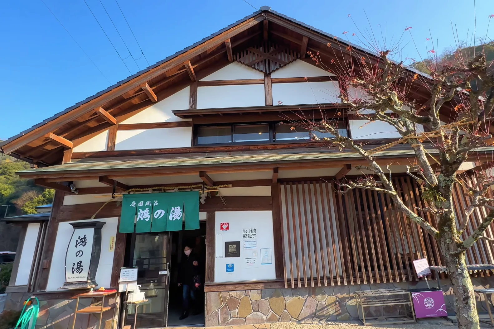 The gabled entrance of Ko-no-yu bathhouse in Kinosaki with its noren and name board.