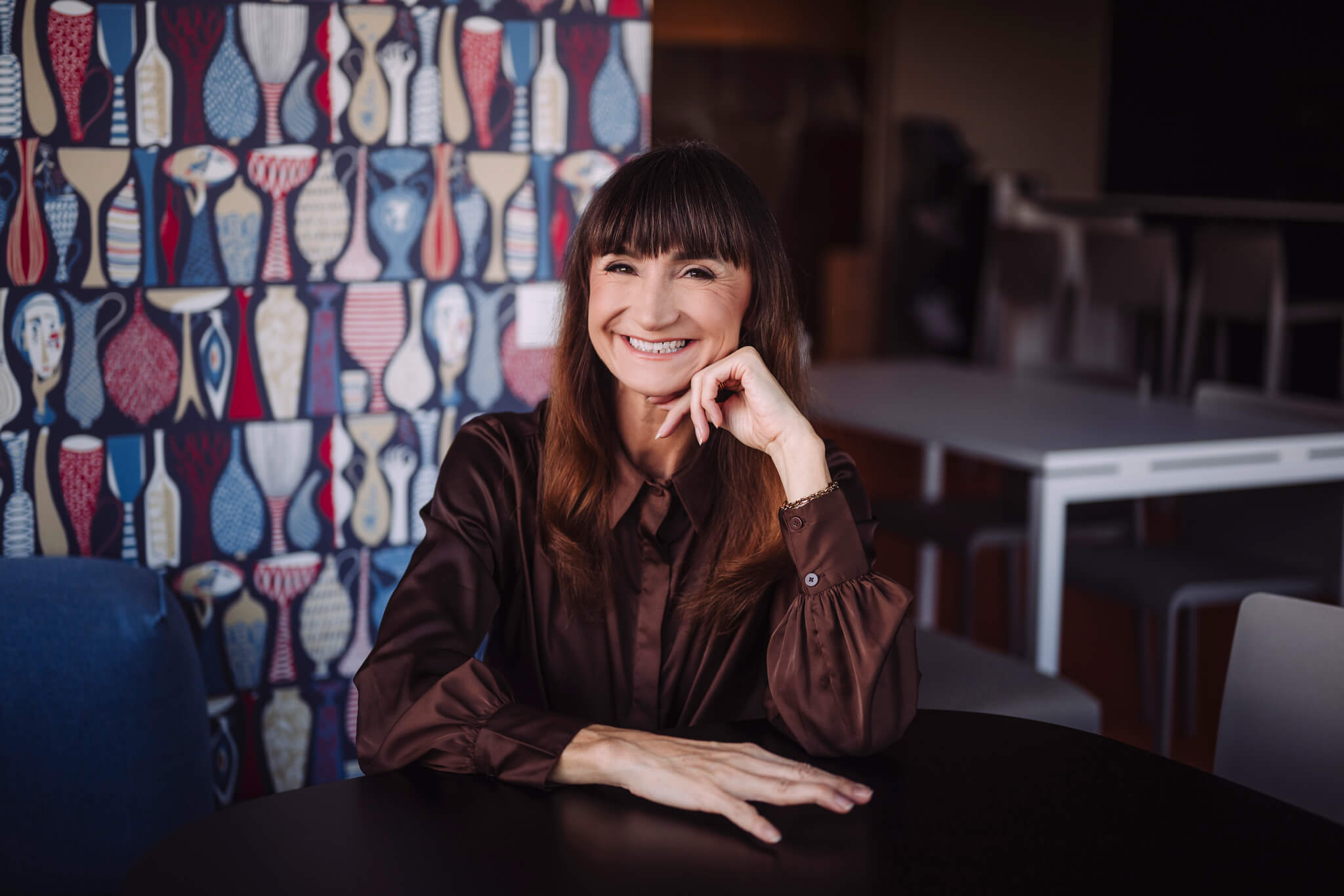Juhtimiscoach Marika Raiski istub laua taga ja naeratab, taustal värviline seinamuster.
