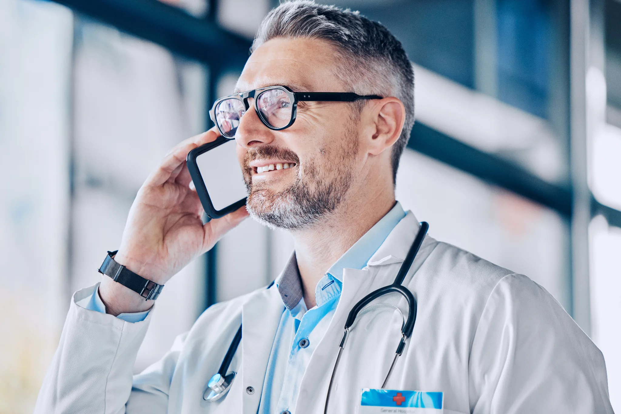 Smiling male physician in white coat with stethoscope talking on a mobile phone