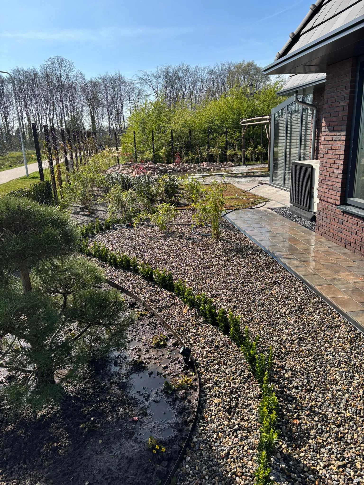 Rustige Japanse tuin met grind, jonge beplanting en een bakstenen huis met airco bij nieuwbouwwoning in Gorredijk.