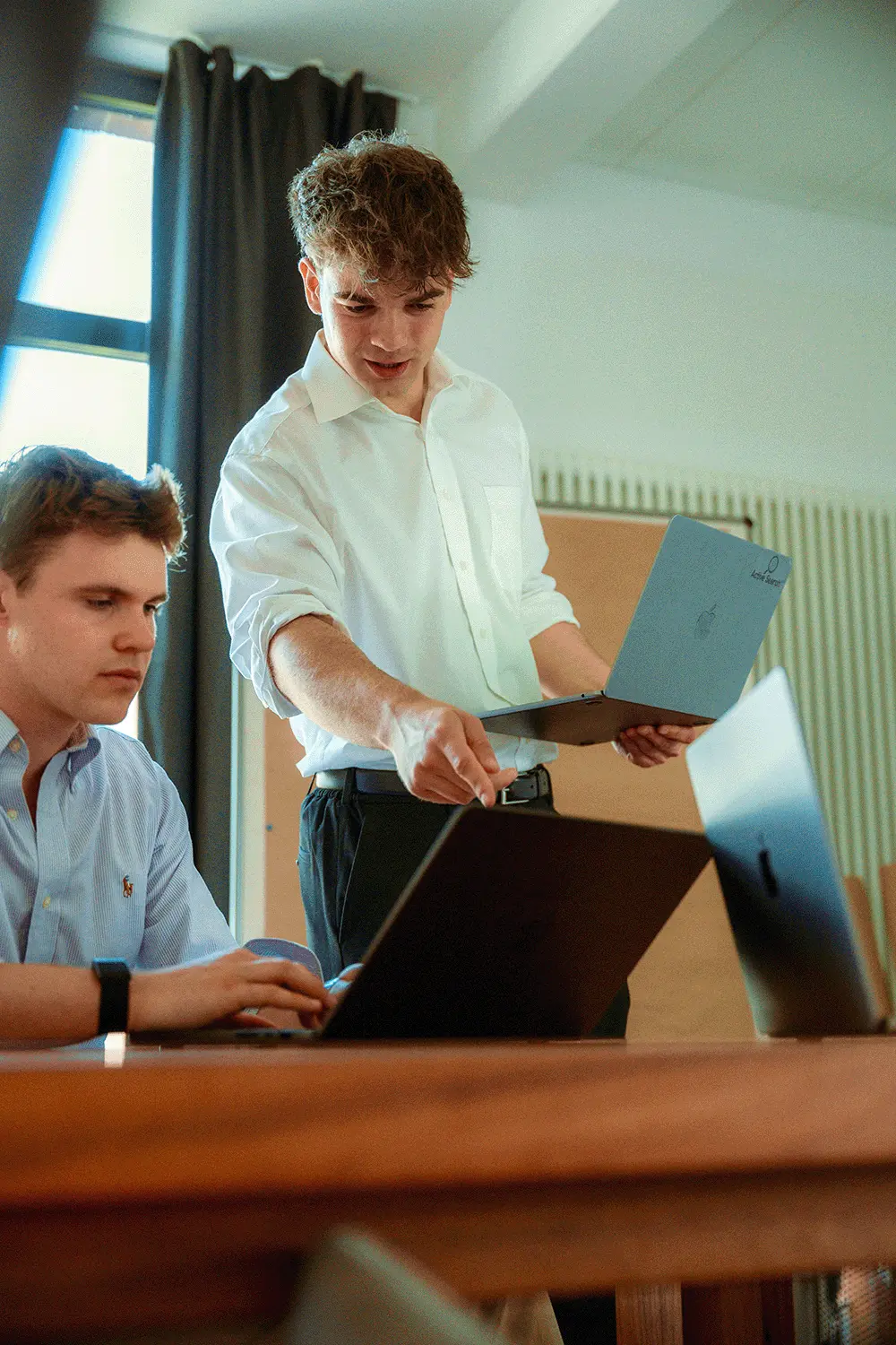 Smiling woman in a beige blouse sitting at a desk with a keyboard in front of a large window