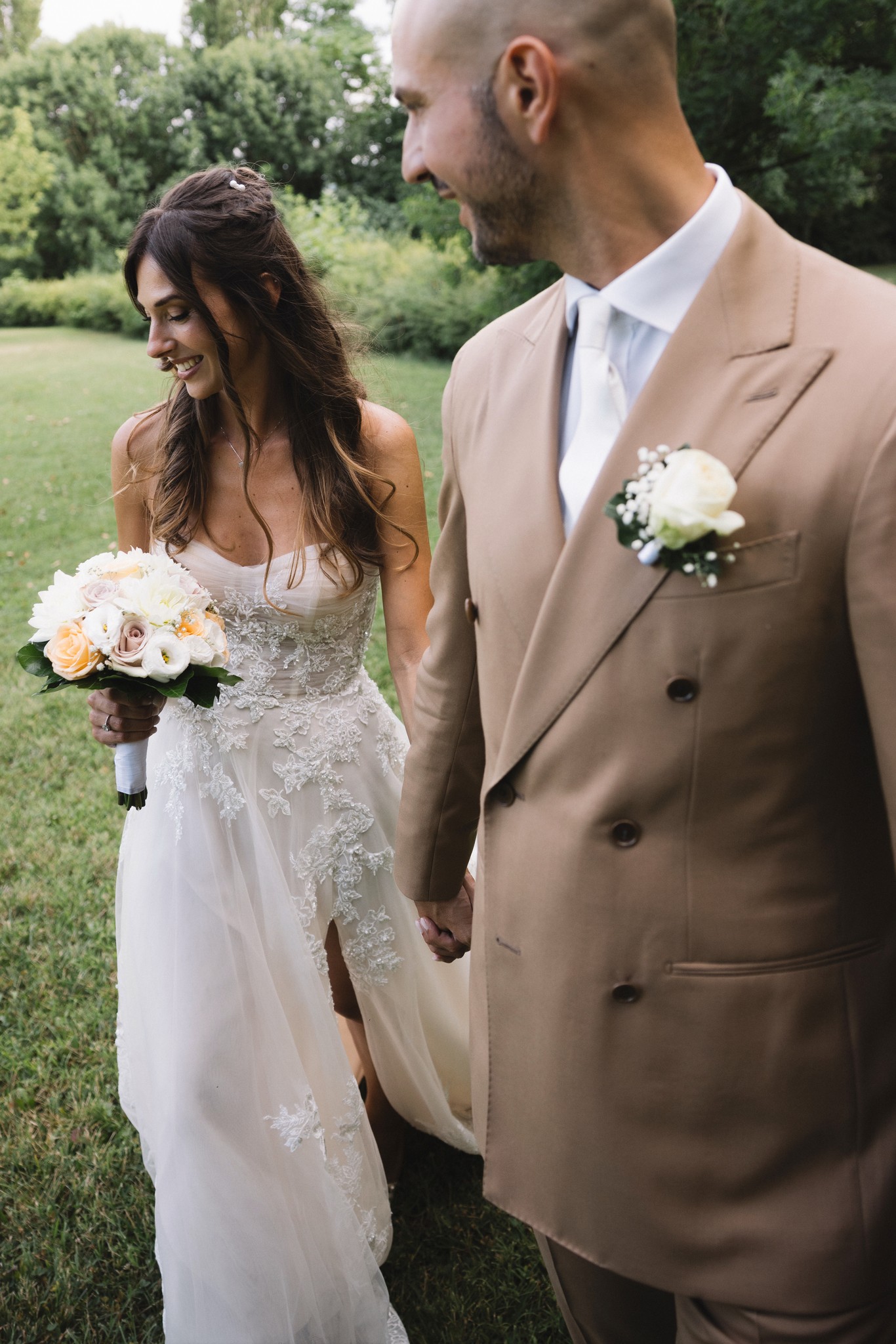 Sposi mano nella mano nel giardino di Villa La Steccata, abito bianco e completo beige, reportage matrimoniale