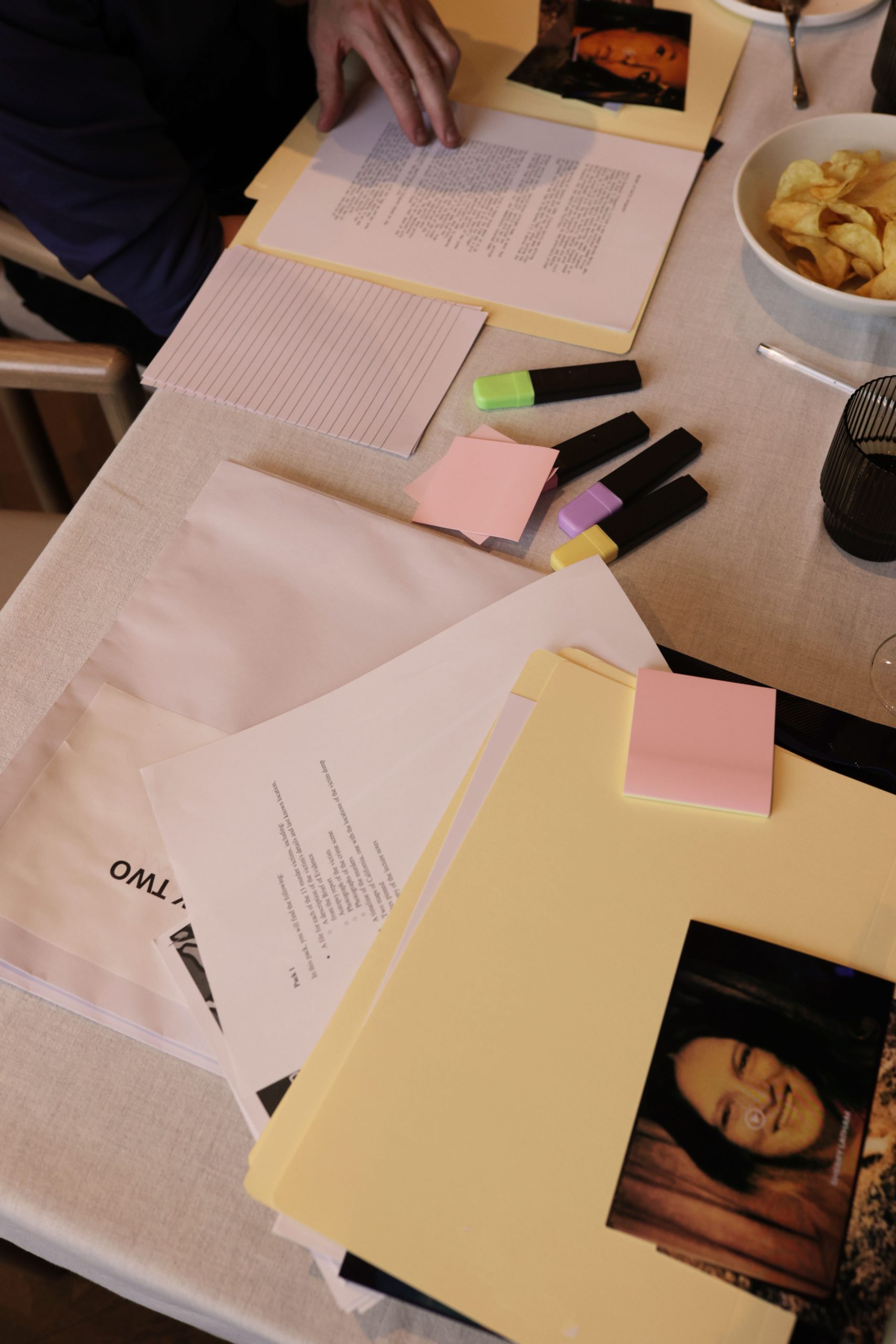 Close-up of case file folders with crime scene photos, notepads and coloured highlighters spread across a table