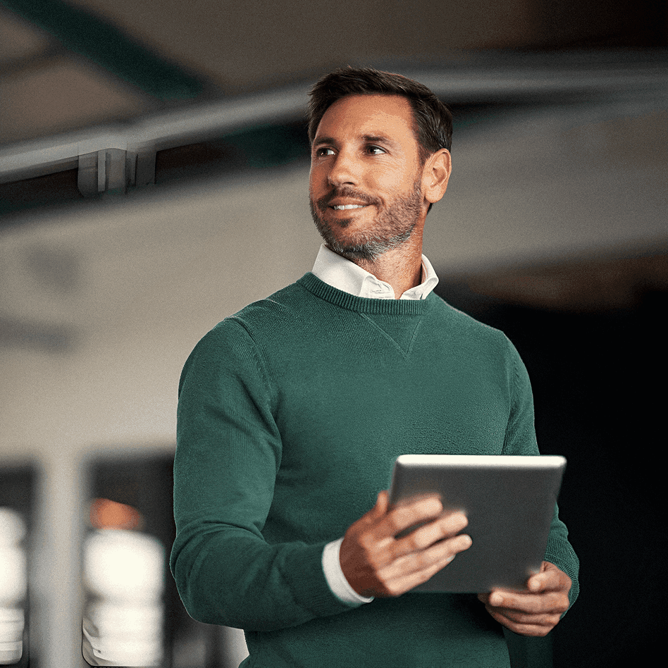 Homem sorridente segurando um tablet em ambiente corporativo.