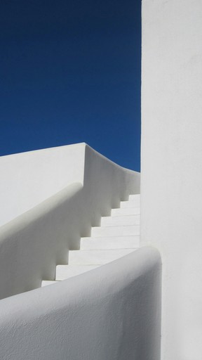 A geometric composition featuring white walls and stairs against a deep blue sky, creating a minimalist aesthetic.