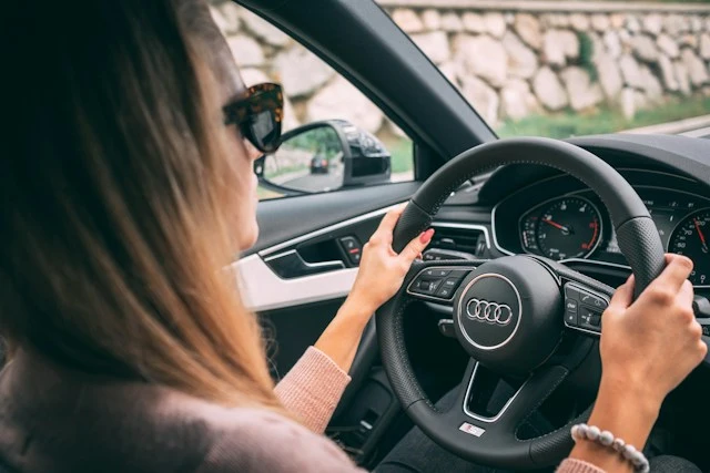 Conductora con gafas de sol al volante de un coche en carretera, representando al conductor habitual que tarifa la póliza de seguro de coche de Allianz en Murcia.